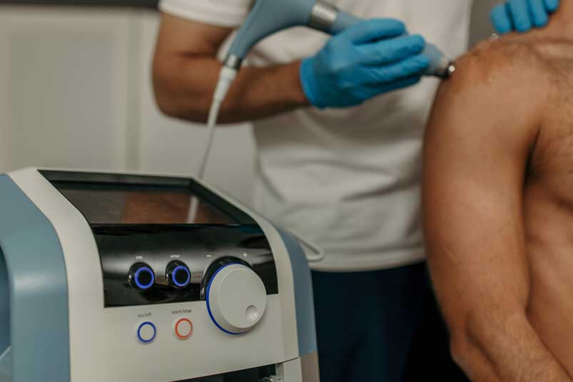 Doctor performing ultrasound therapy on male patient's shoulder in clinic
