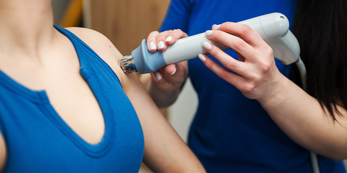 A woman receives treatment with an shockwave ESWT device applied to her arm, related to an ESWT machine buying checklist.