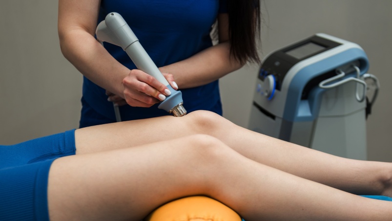 A clinician using a professional shockwave therapy system to treat a patient's knee